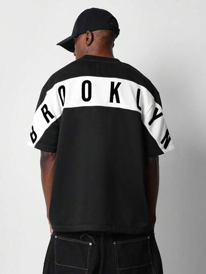 SUMWON قميص جرافيك كاجوال بطباعة خلفية أوفر سايز بشعار الألوان الرياضية بأسلوب فارسيتي للموضة الحضرية للشارع في برووكلين