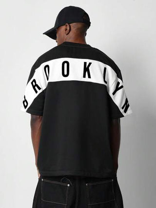 SUMWON قميص جرافيك كاجوال بطباعة خلفية أوفر سايز بشعار الألوان الرياضية بأسلوب فارسيتي للموضة الحضرية للشارع في برووكلين