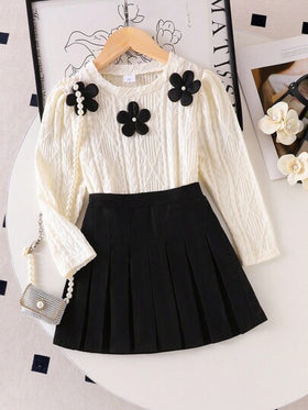 SHEIN Elladie kids طقم تي شيرت وتنورة صغيرة سوداء مريحة للفتيات الصغيرات، التي تتكون من بلوزة بياقة دائرية وأكمام طويلة بطبعات زهور بيضاء، مقترنة بتنورة سوداء مطوية
