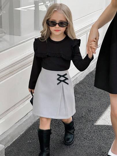 SHEIN Elladie kids طقم تي شيرت وتنورة للفتيات الصغيرات، التي تتكون من ملابس علوية سوداء طويلة الأكمام مزينة بالكشكشة مع تنورة مزينة بفيونكة وذات حافة مشقوقة، مناسب للخريف والشتاء